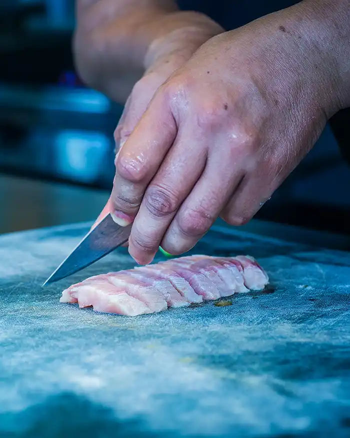 Chef découpant du poisson cru en fines tranches régulières pour un ceviche