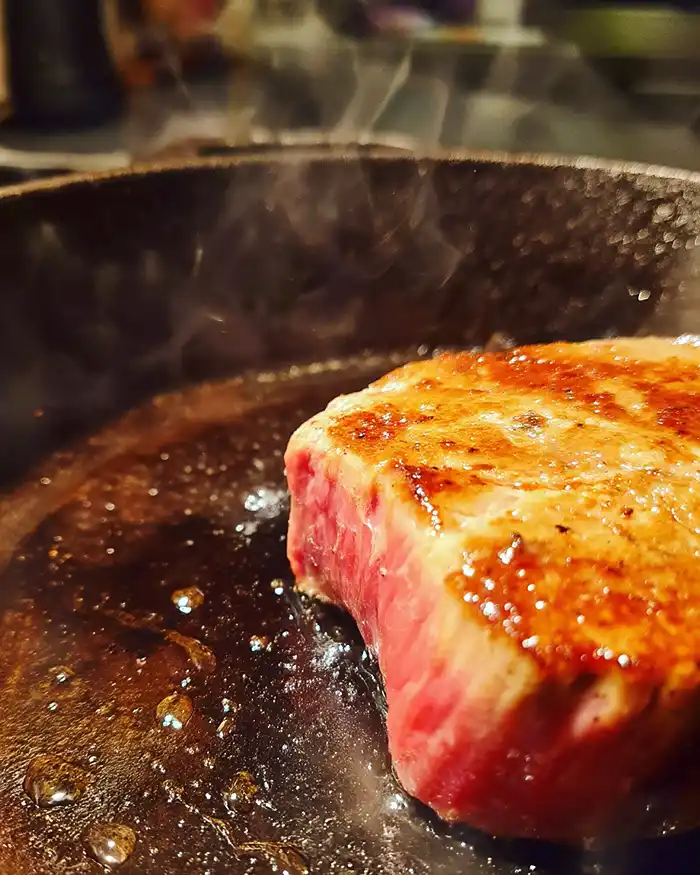 Recettes Tatakis et Viandes Mi-cuites 2 Filet de boeuf en train d'être saisi à feu vif dans une poêle en fonte pour un tataki parfait